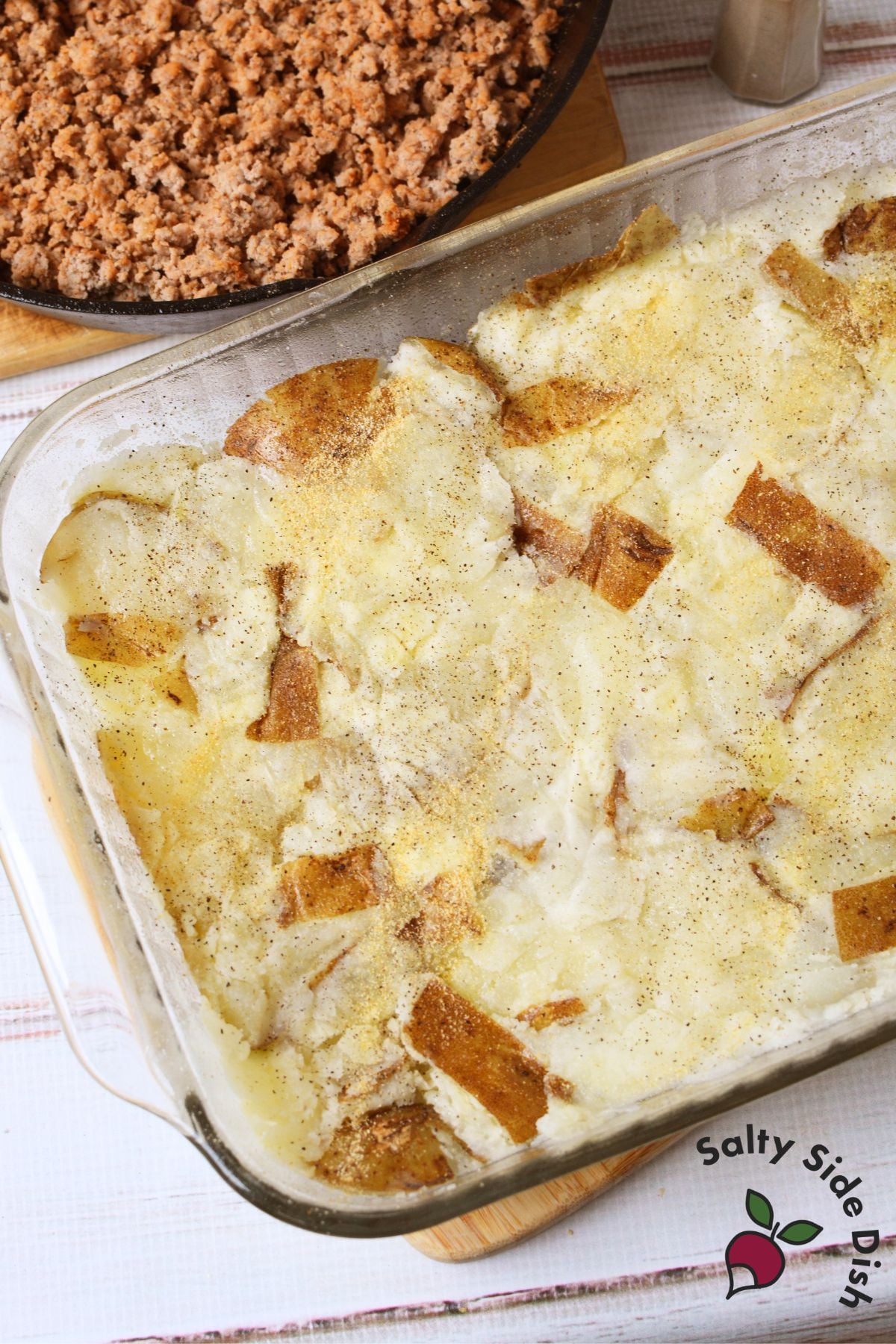 Baked potato crust in glass dish with cooked ground turkey in skillet nearby