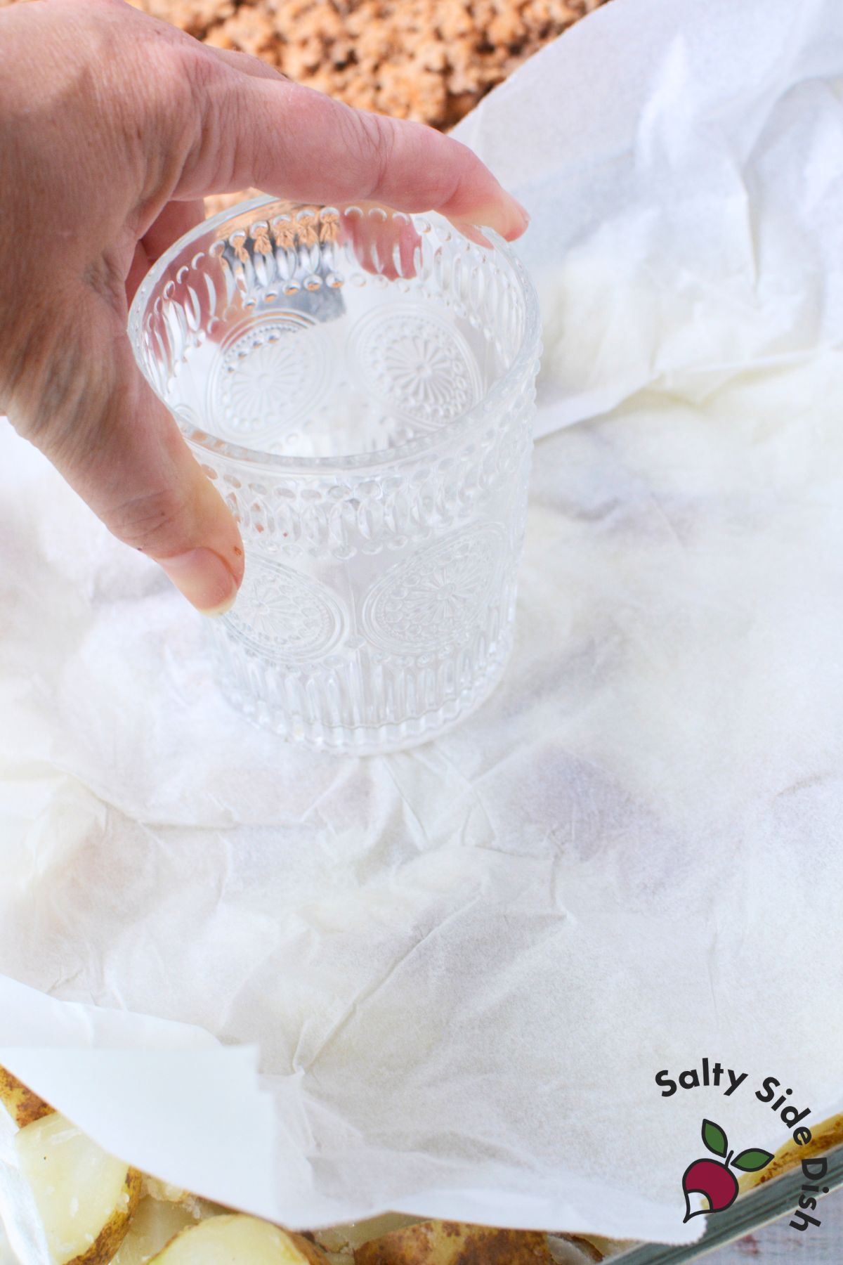 Pressing boiled potatoes into baking dish with a glass over parchment paper