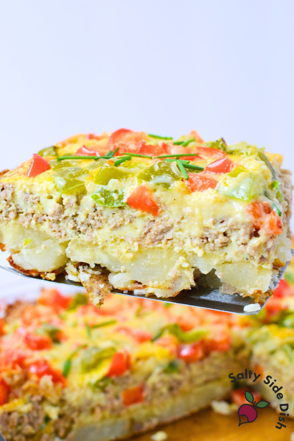 Spatula lifting a slice of breakfast potato casserole showing potato, turkey and egg layers