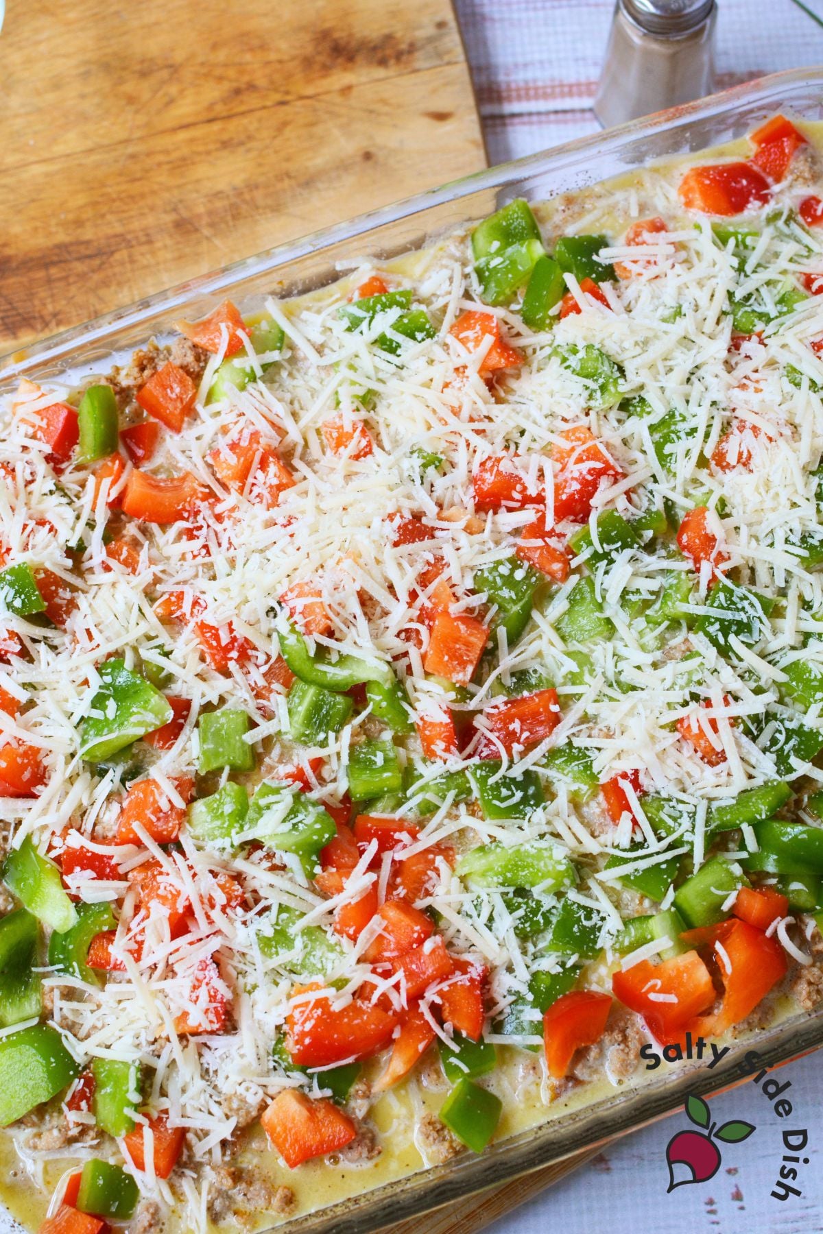 Unbaked casserole topped with chopped bell peppers and shredded Parmesan cheese