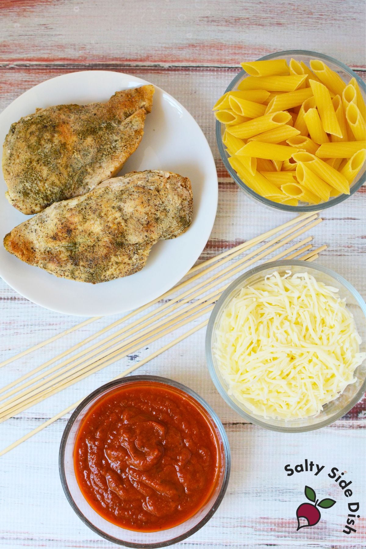Ingredients for chicken Parmesan pasta skewers including cooked chicken, penne, marinara, mozzarella, and wooden skewers
