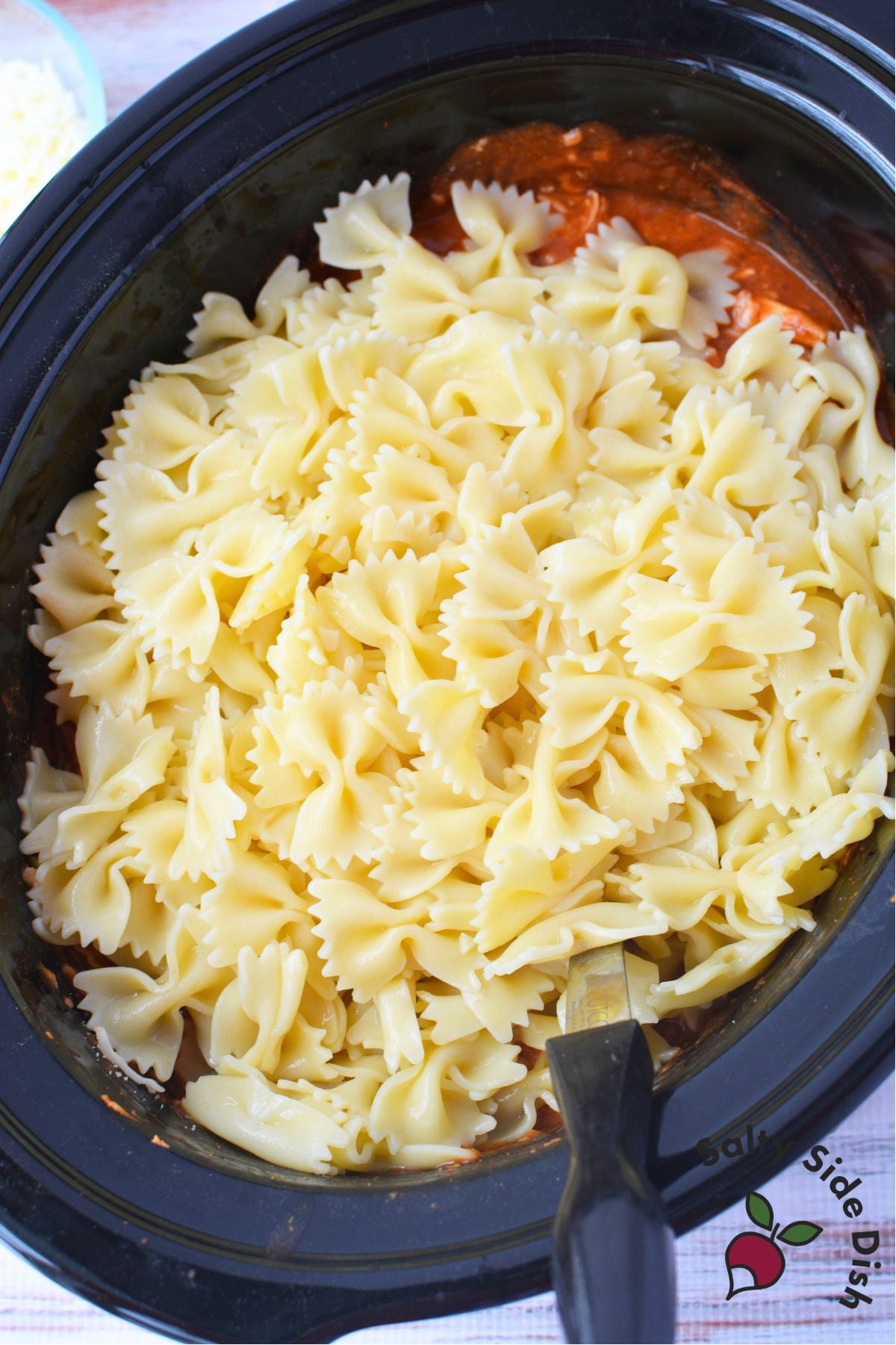 Cooked farfalle pasta added to pink sauce chicken in the slow cooker
