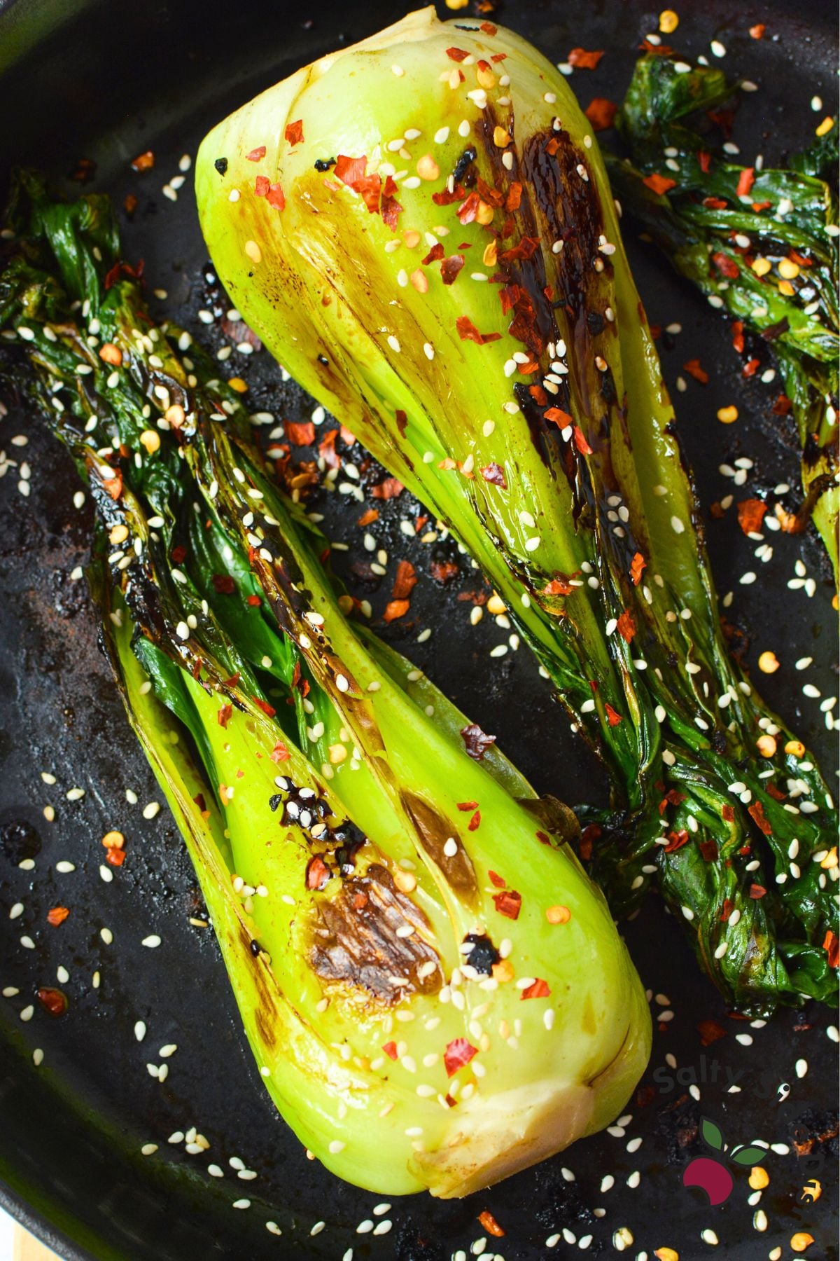Close-up of sautéed bok choy with browned edges, sesame seeds, and red pepper flakes