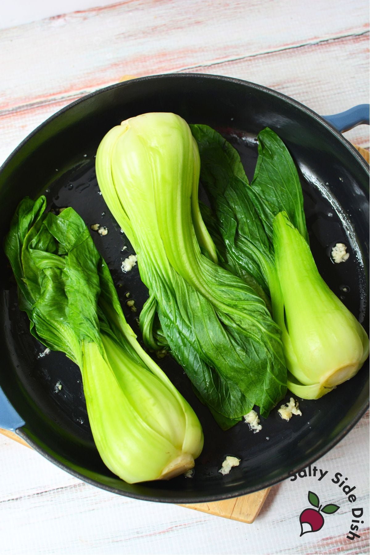 Baby bok choy and minced garlic cooking in a skillet