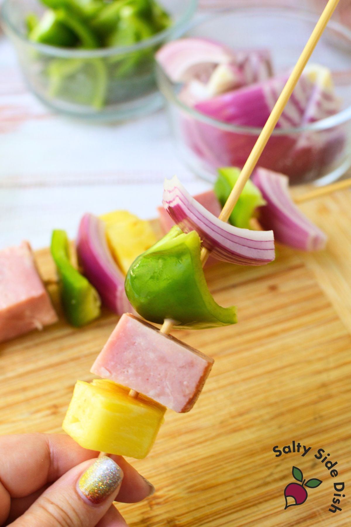 Assembling grilled ham and pineapple kabobs with pineapple, ham, green pepper and red onion