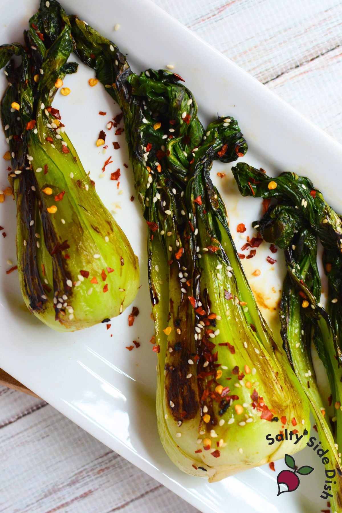 Sautéed bok choy with garlic, sesame seeds, and crushed red pepper served on a white platter