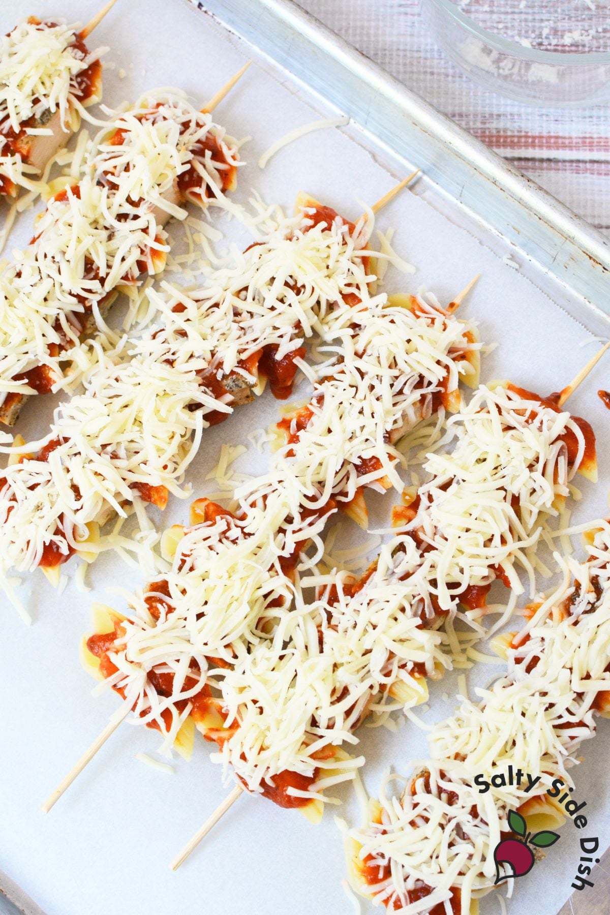 Chicken Parmesan pasta skewers topped with marinara and shredded mozzarella before baking