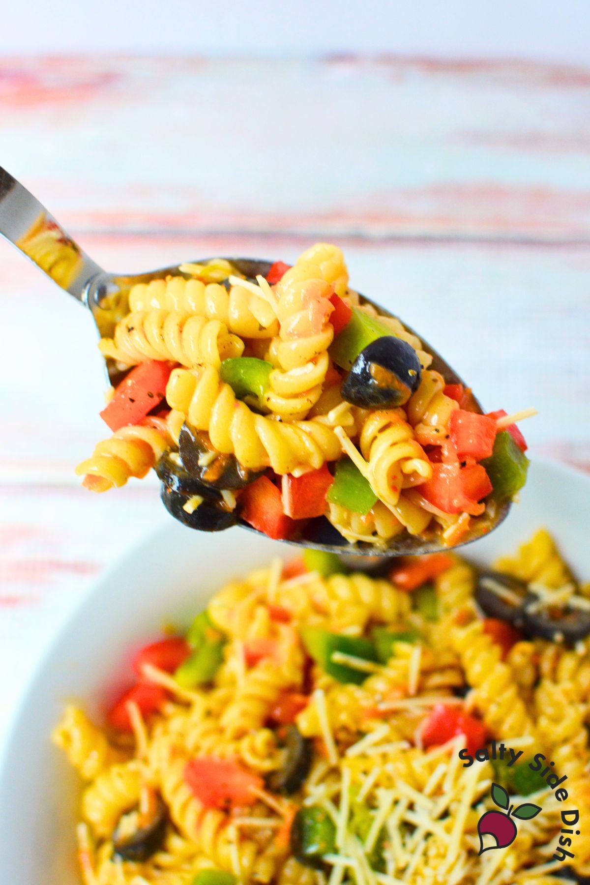 Spoonful of rotini pasta salad with bell peppers, black olives, carrots, and Parmesan cheese