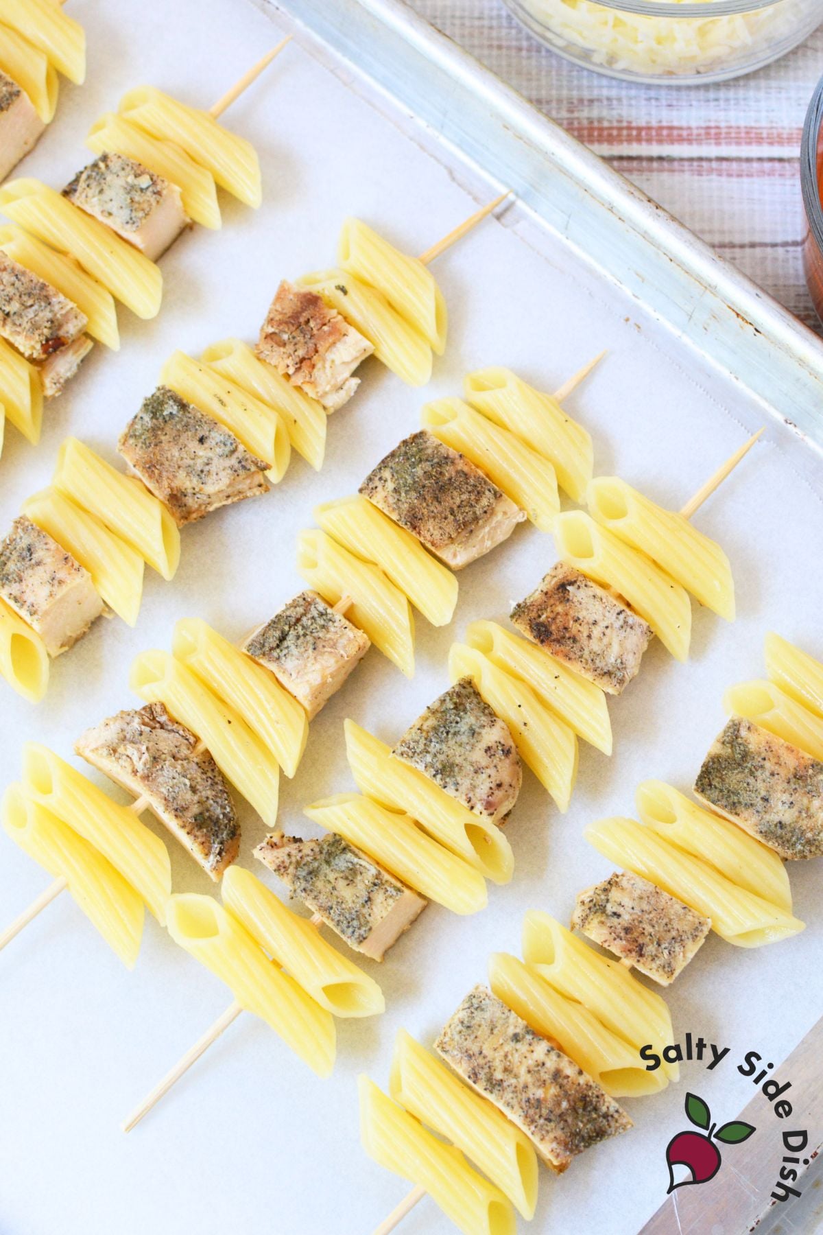 Chicken and penne pasta skewers arranged on a parchment-lined baking sheet