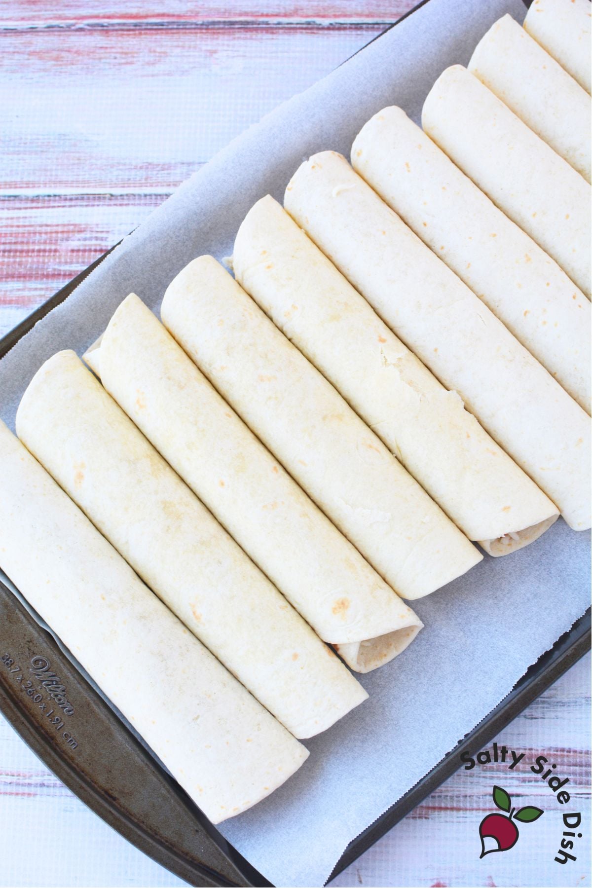 Rolled flour tortillas arranged seam side down on a parchment lined baking sheet