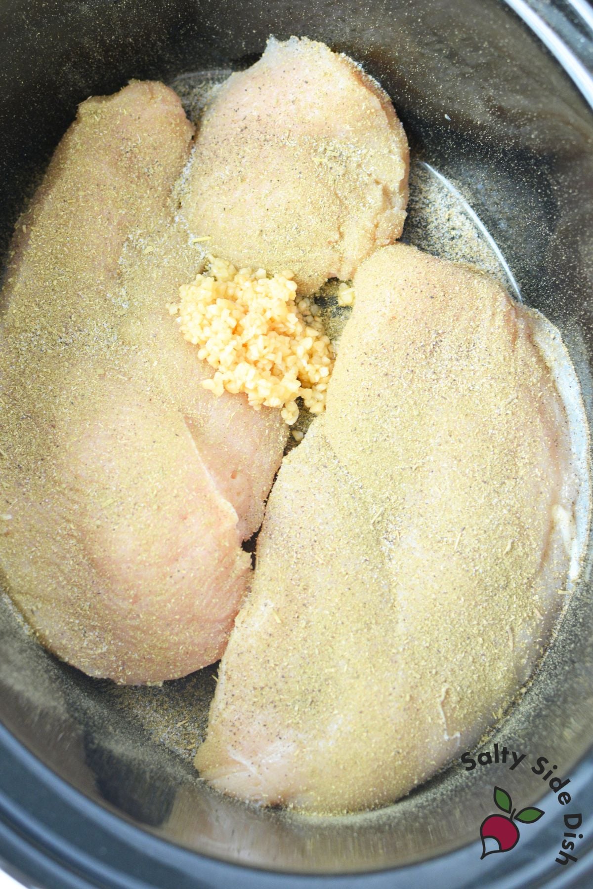 Seasoned chicken breasts with minced garlic in a slow cooker