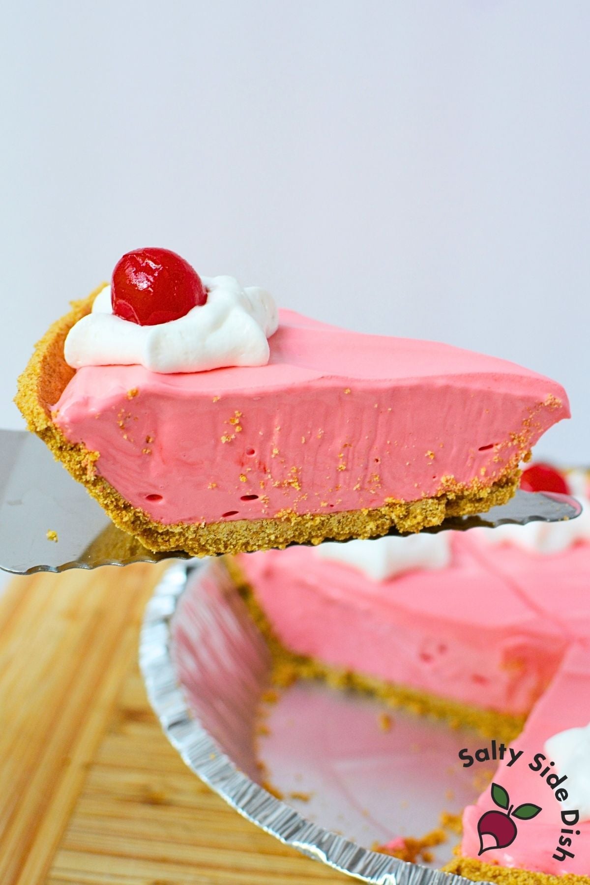 Slice of Kool Aid pie on a pie server showing the creamy cherry filling and graham cracker crust