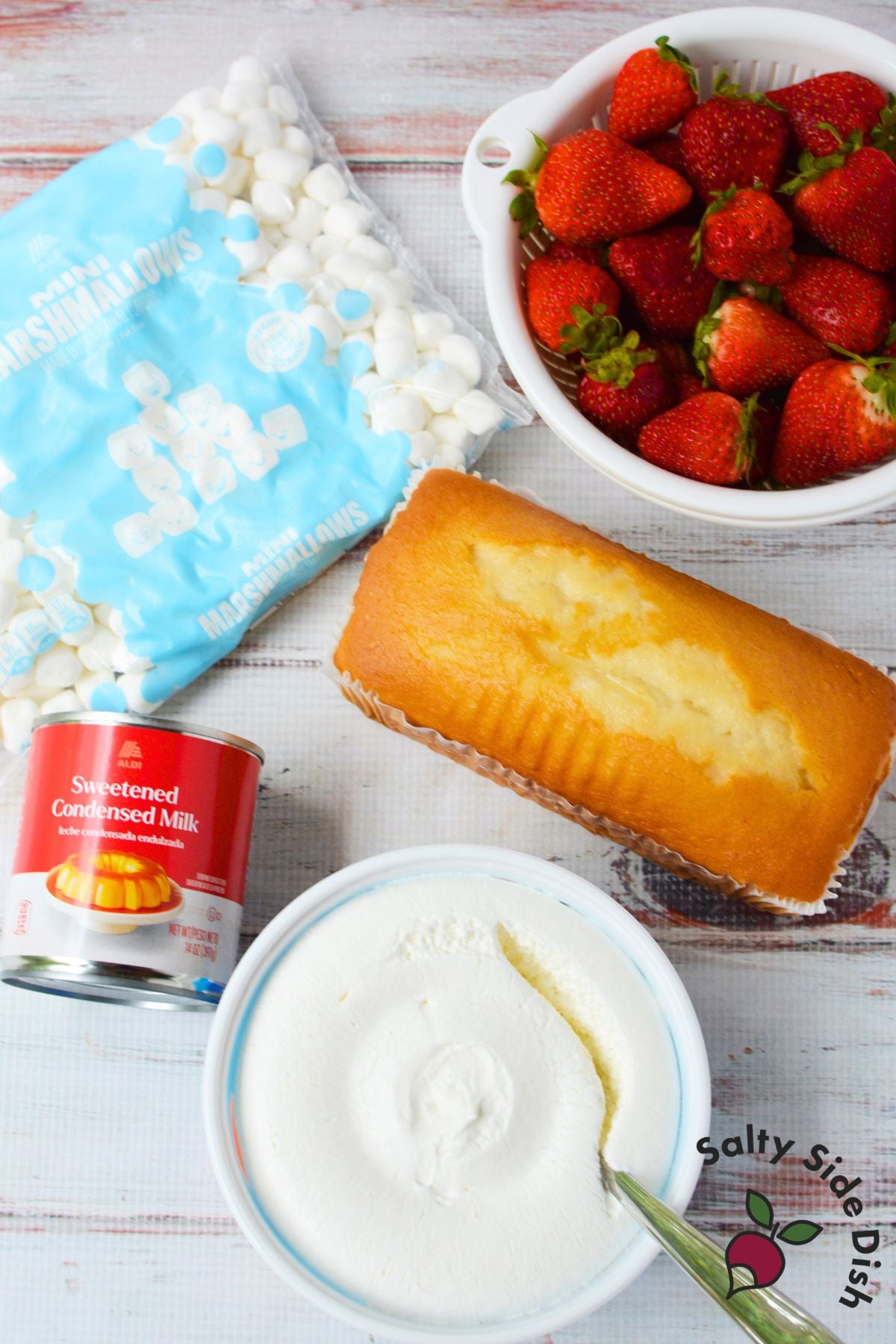 Ingredients for strawberry shortcake fluff salad including strawberries, pound cake, mini marshmallows, whipped topping, and condensed milk