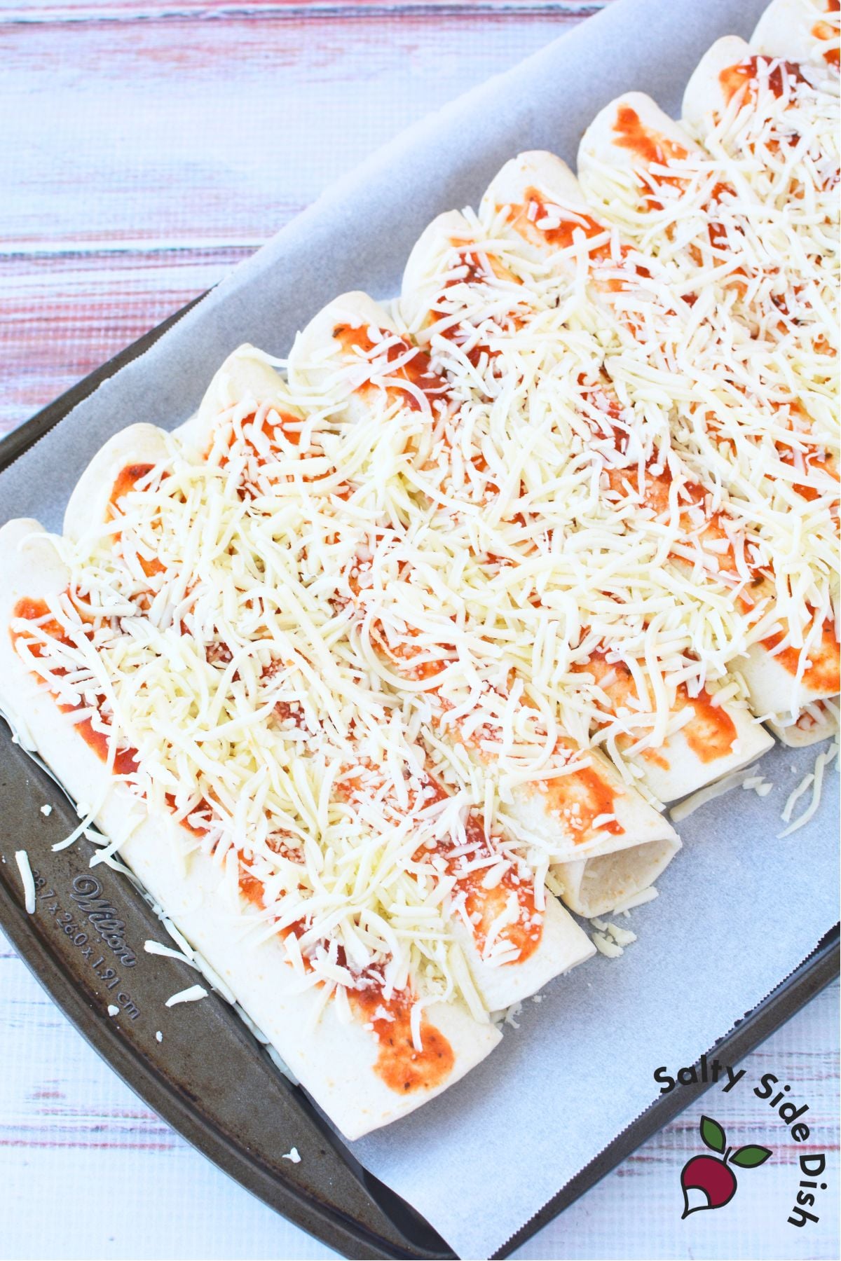 Unbaked lasagna rolls with tortillas topped with pasta sauce and shredded mozzarella