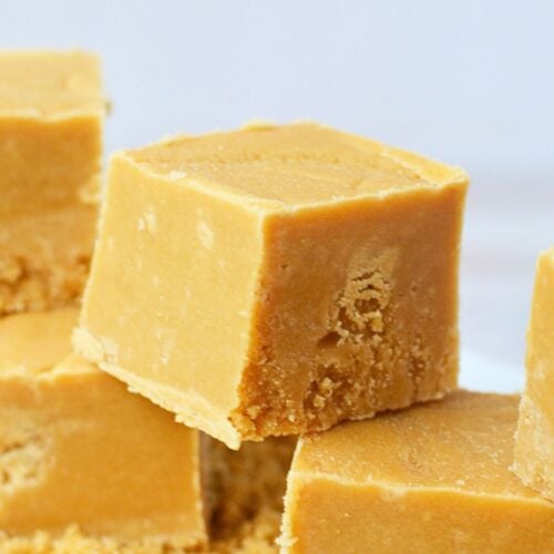 Close-up of smooth brown sugar fudge squares stacked over loose brown sugar.