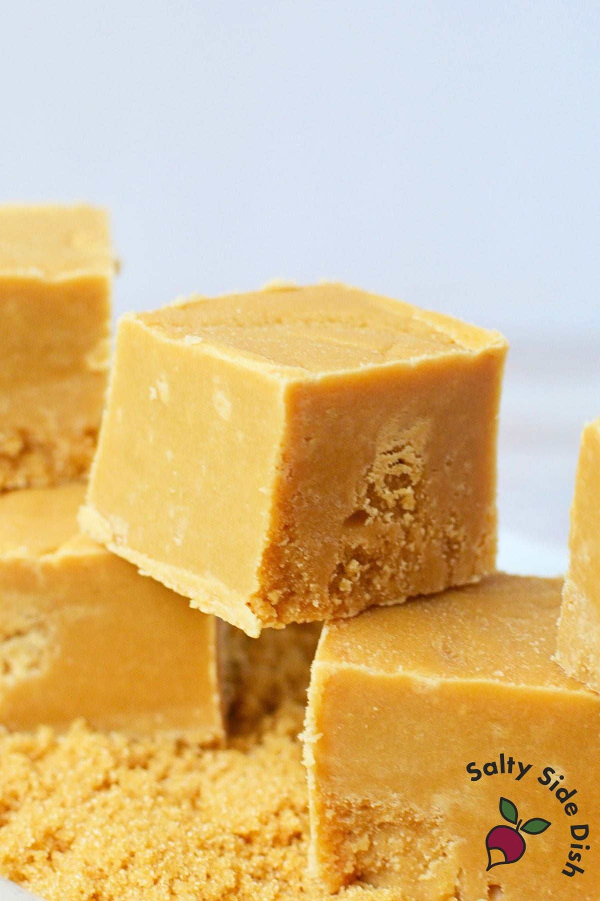 Close-up of smooth brown sugar fudge squares stacked over loose brown sugar.