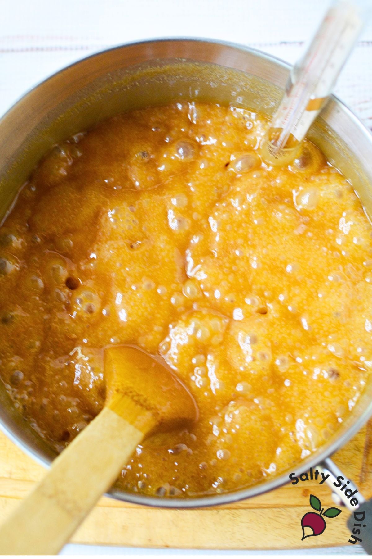 Brown sugar fudge mixture boiling in a saucepan with a candy thermometer inserted to check the temperature.