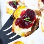 Cranberry Brie smashed potato lifted on a spatula, showing the creamy potato, melted Brie, cranberry sauce, and rosemary topping.