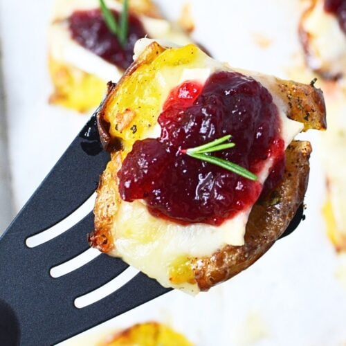 Cranberry Brie smashed potato lifted on a spatula, showing the creamy potato, melted Brie, cranberry sauce, and rosemary topping.