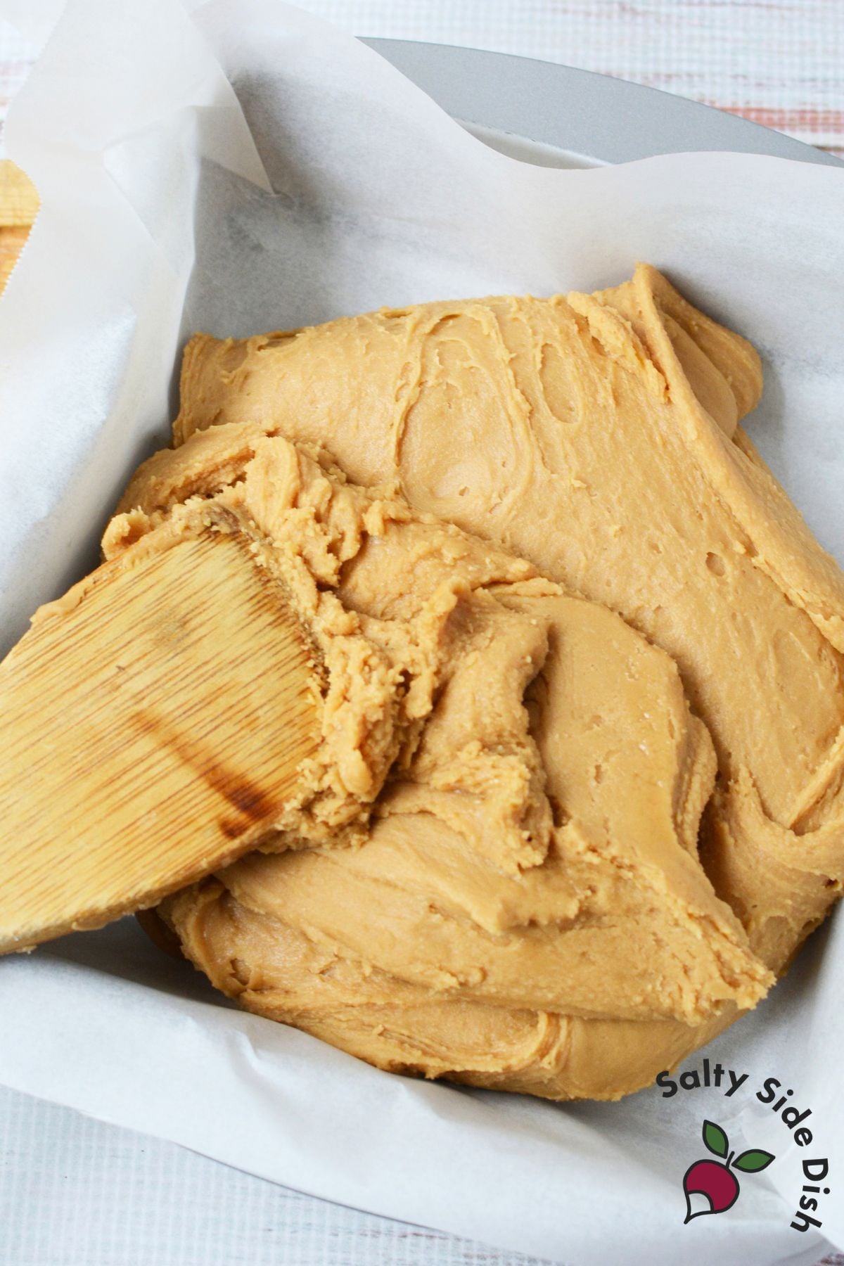 Thick brown sugar fudge mixture being spread into a parchment-lined baking pan.