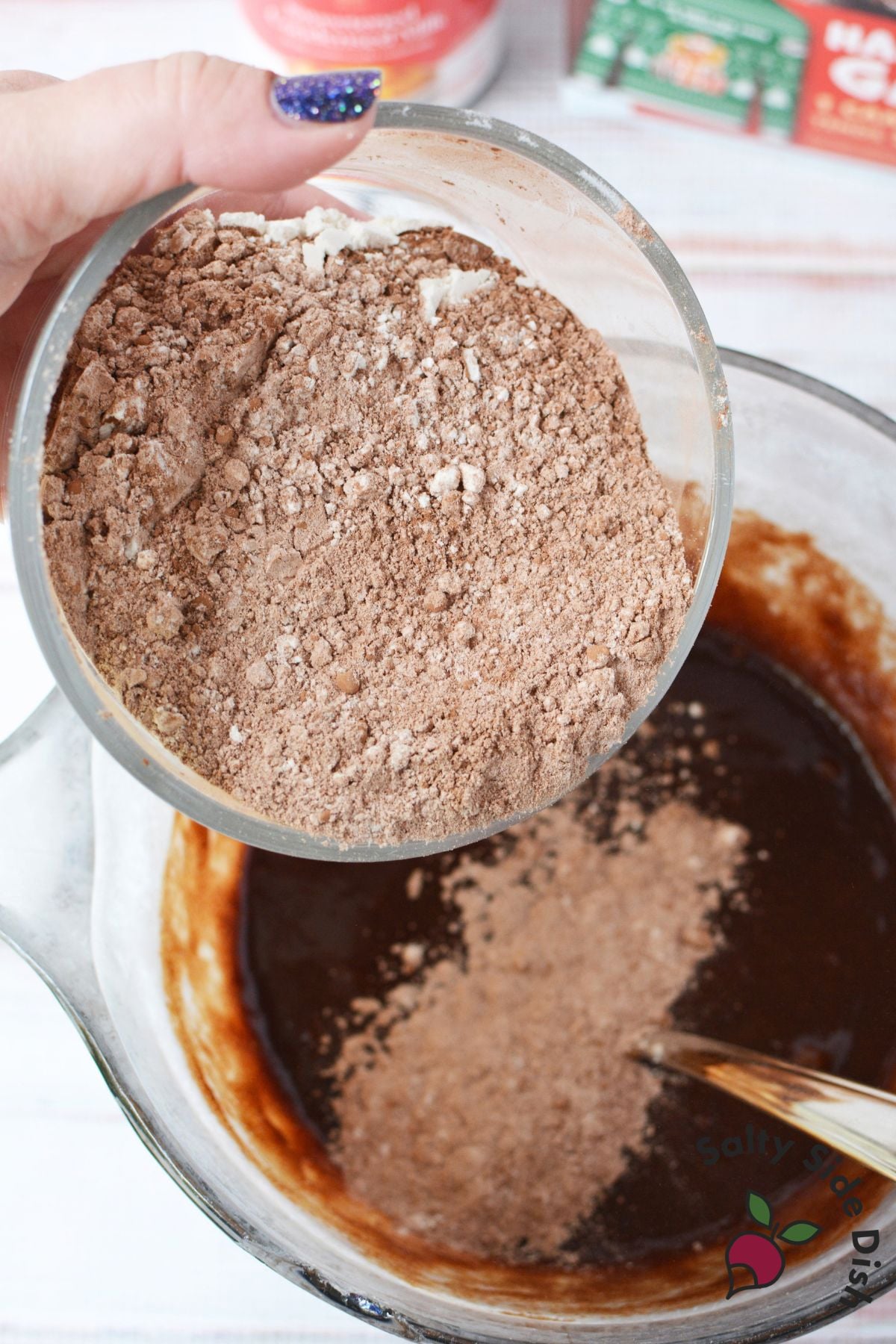Cocoa and flour mixture being added to melted chocolate brownie batter in a mixing bowl.