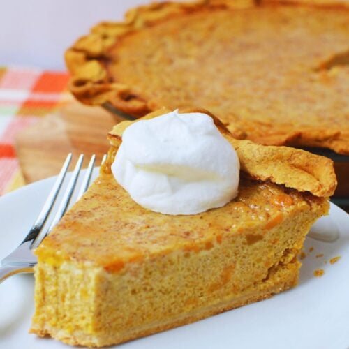 Slice of butternut squash and sweet potato pie topped with whipped cream.