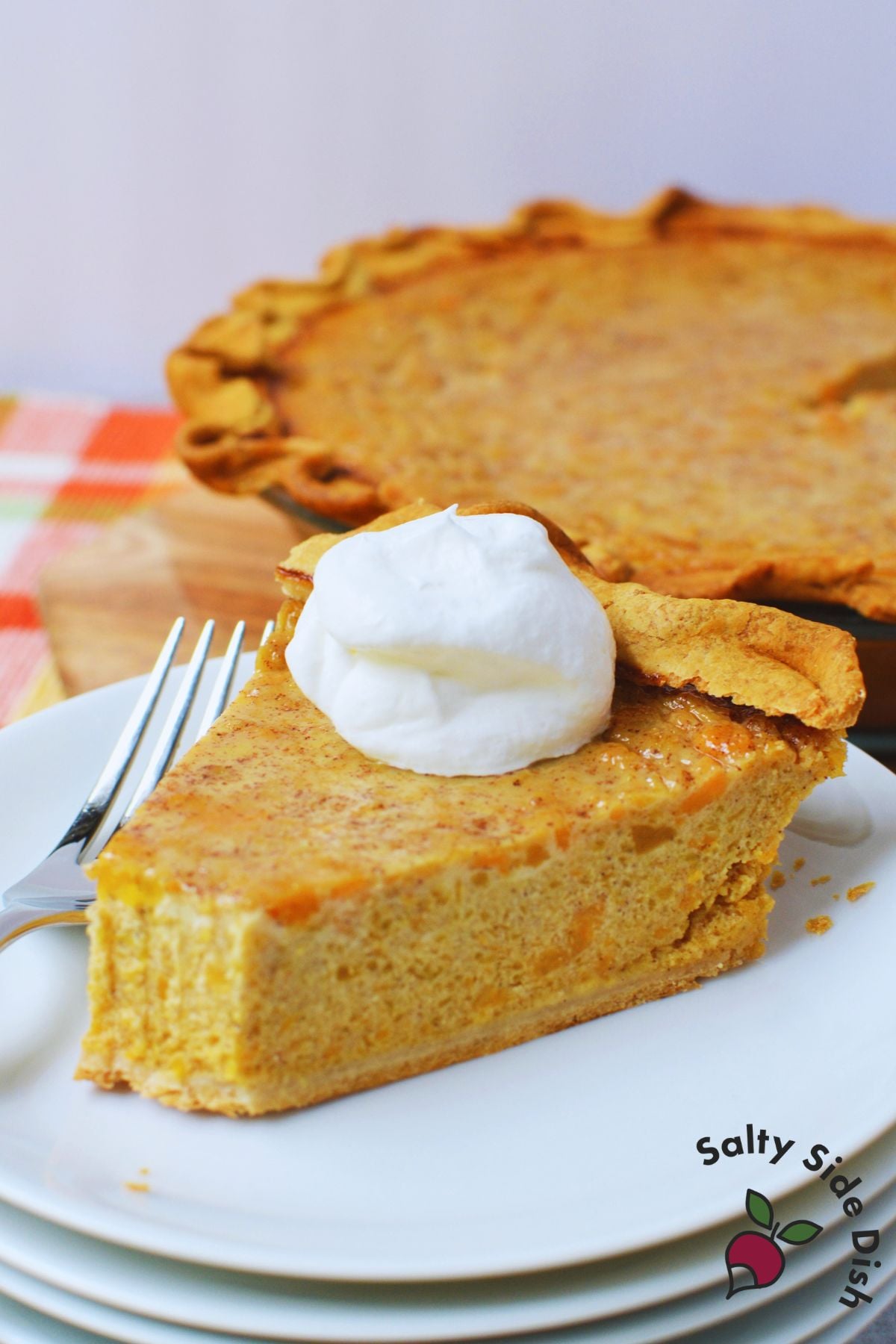 Slice of butternut squash and sweet potato pie topped with whipped cream.