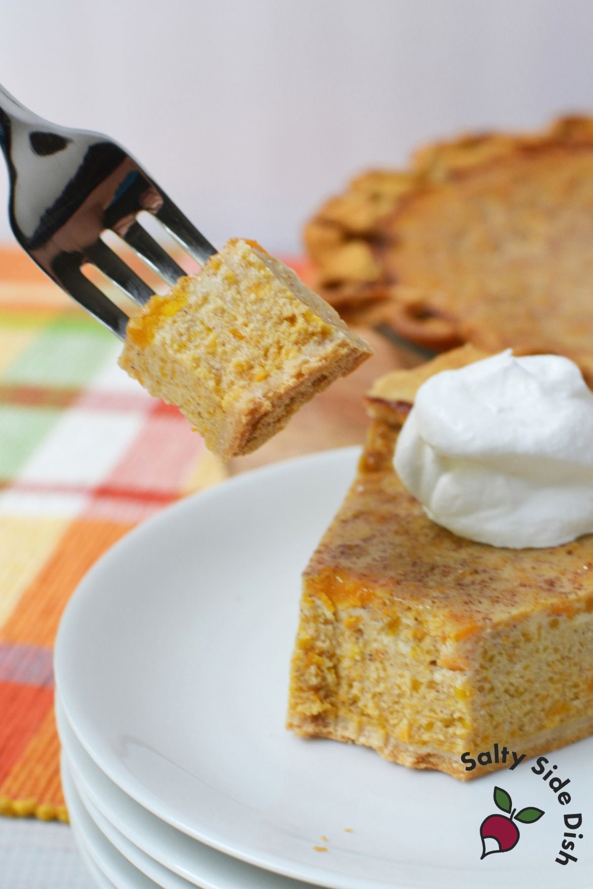 Bite-sized piece of butternut squash and sweet potato pie lifted on a fork beside a slice topped with whipped cream.