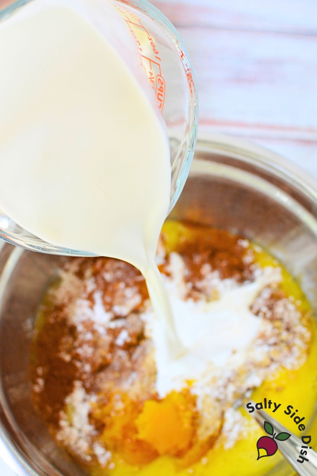 Half-and-half being poured into the butternut squash and sweet potato pie filling with spices and mashed vegetables.