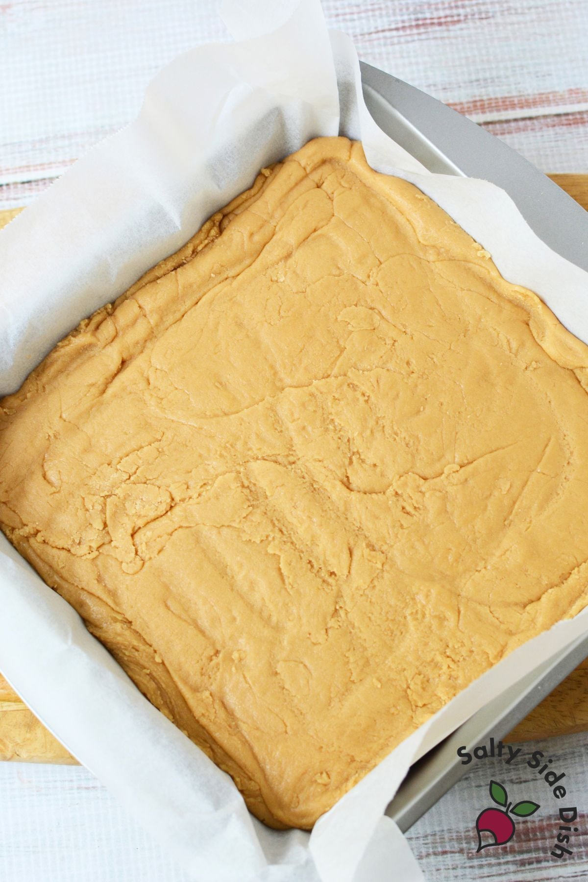 Brown sugar fudge pressed into a parchment-lined 8x8 baking pan before cooling and slicing.