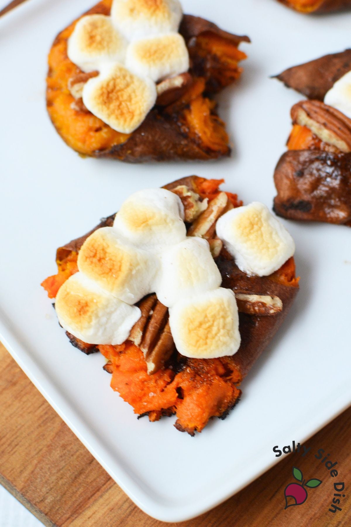 Smashed sweet potatoes topped with toasted mini marshmallows and pecans on a white serving platter