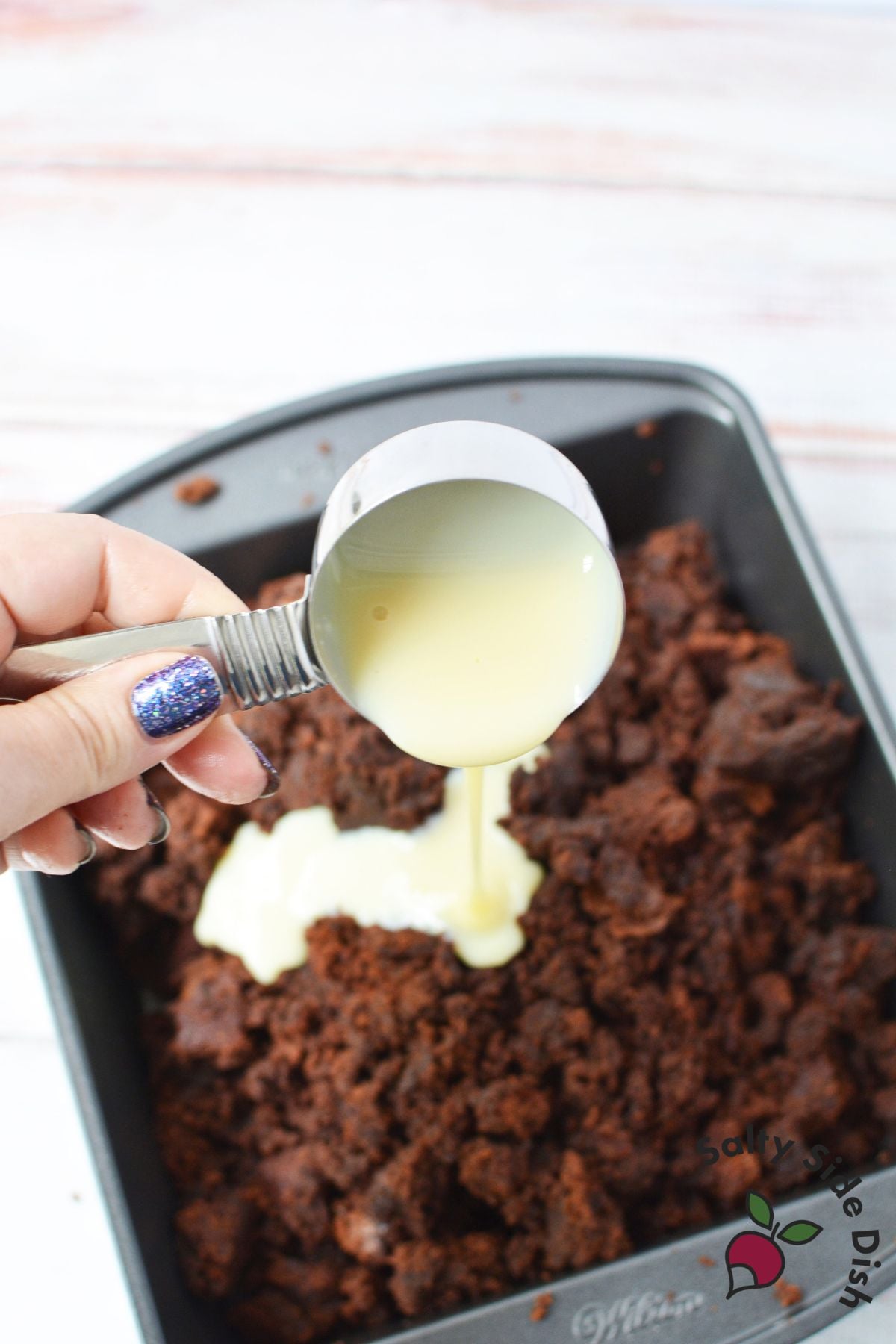 Sweetened condensed milk being poured over crumbled brownies before shaping the pinecones.