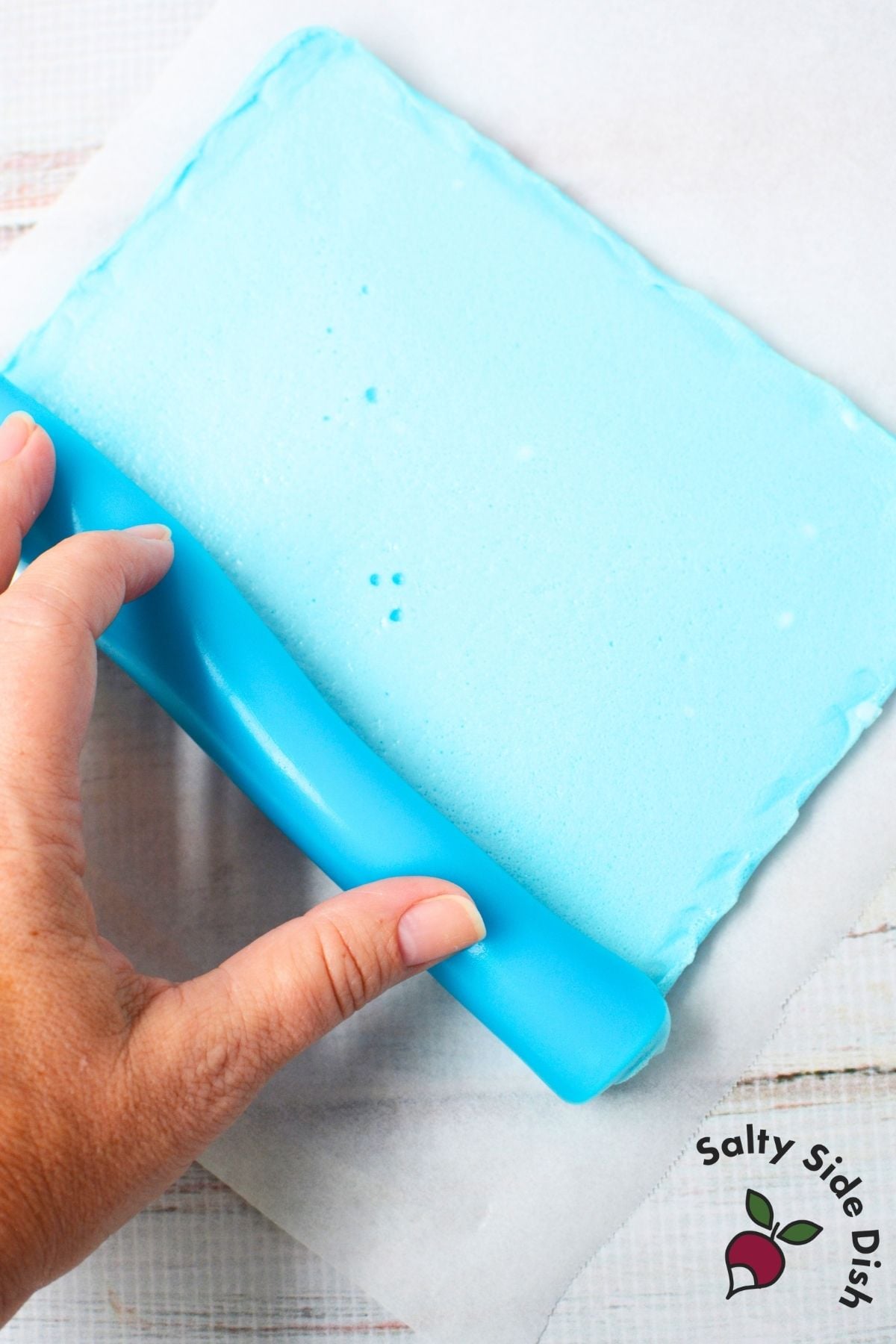 Blue Jello sheet being rolled into a log on parchment paper for homemade Jello roll ups
