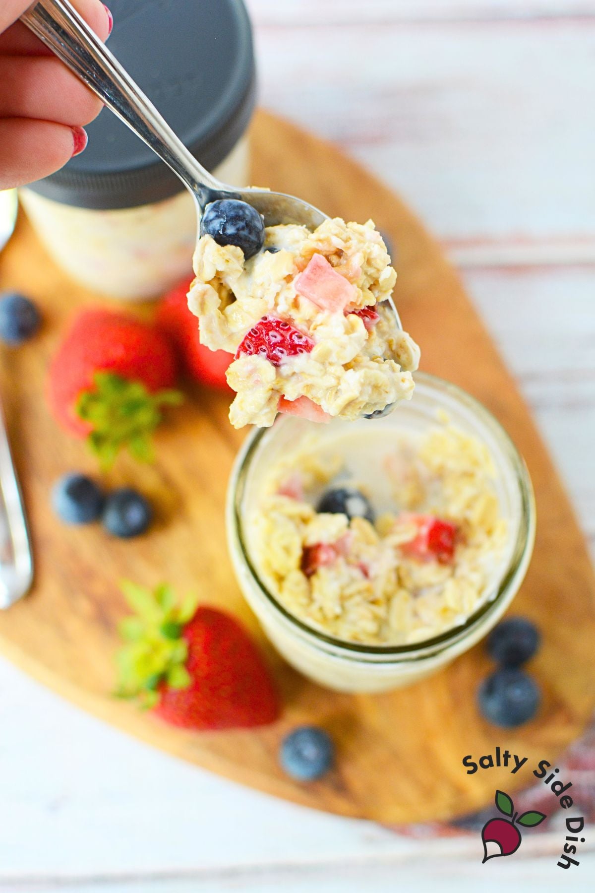 Spoonful of creamy berry overnight oats with strawberries and blueberries above a mason jar.