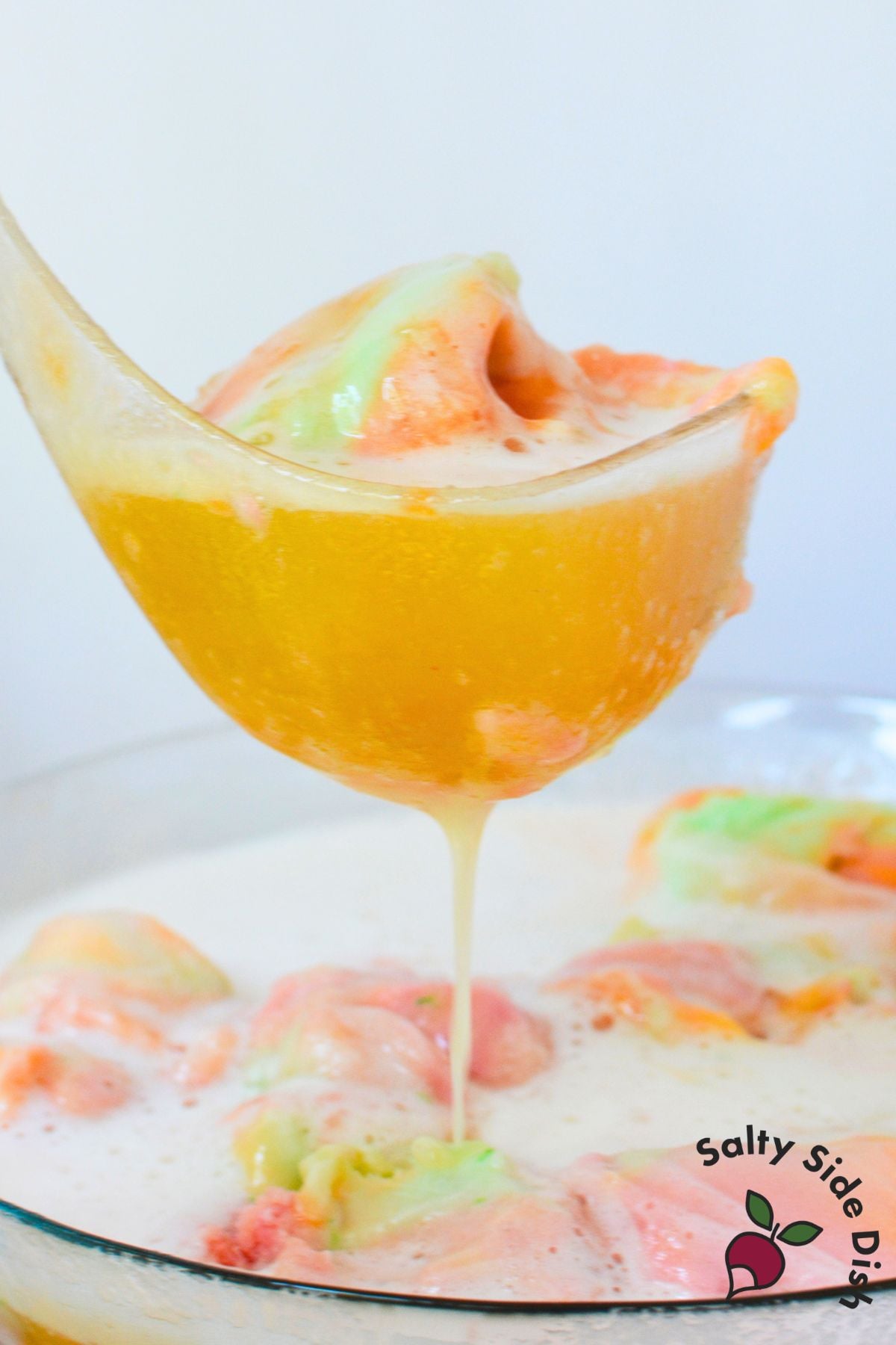 Ladle filled with fruity rainbow sherbet punch from a large punch bowl