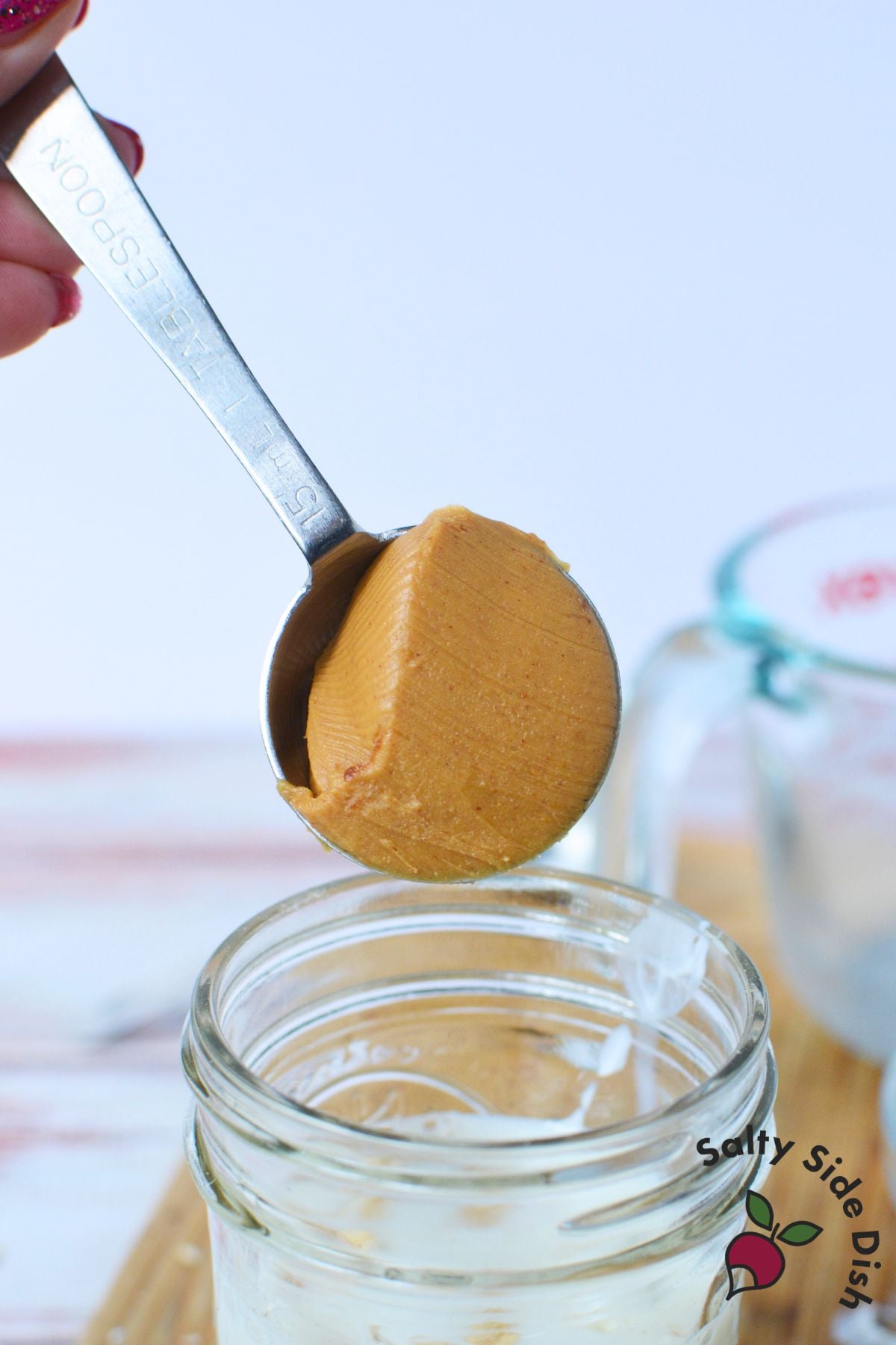 Tablespoon of peanut butter being added to a mason jar to make chocolate peanut butter overnight oats.