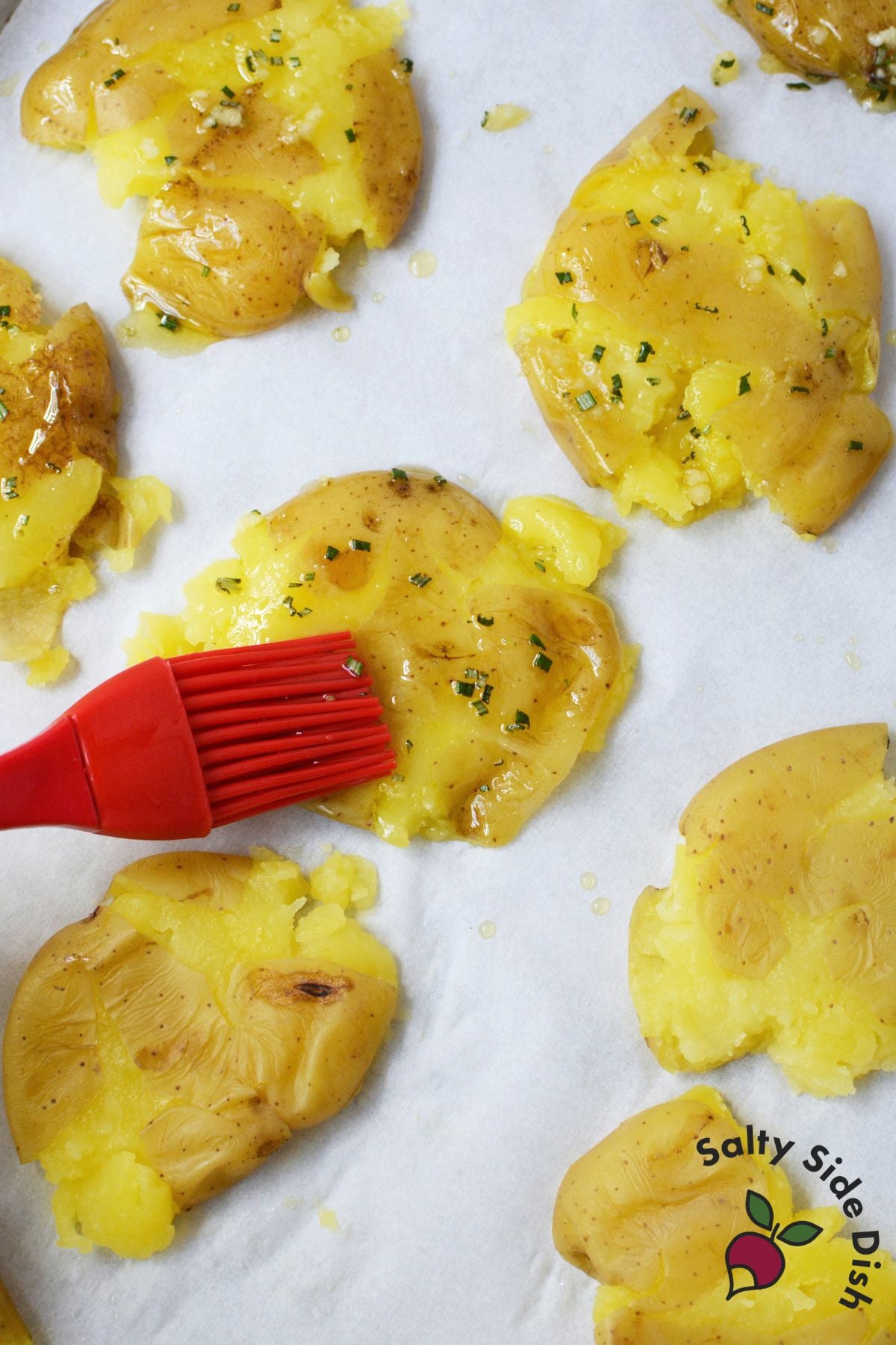garlic rosemary olive oil being brushed over smashed baby gold potatoes before roasting.