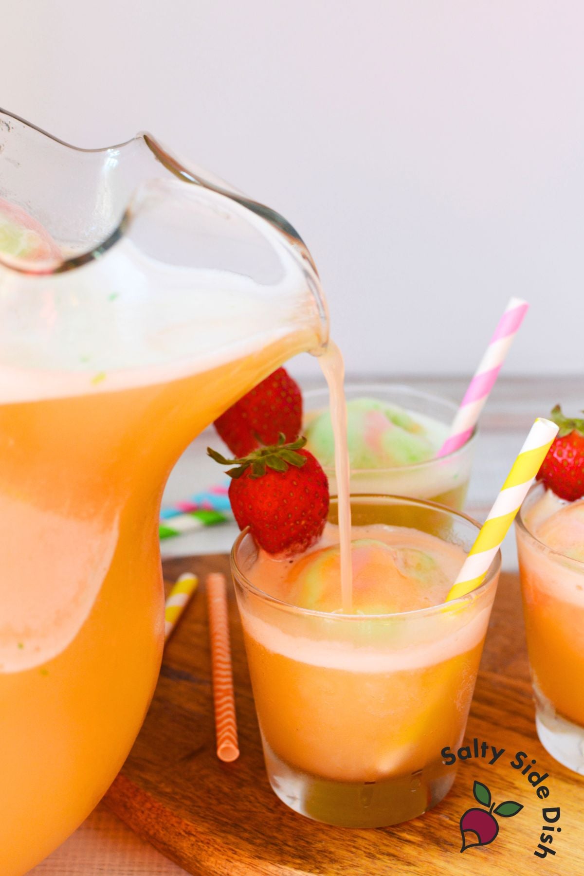 Rainbow sherbet punch poured from a pitcher into party glasses with strawberries and colorful straws