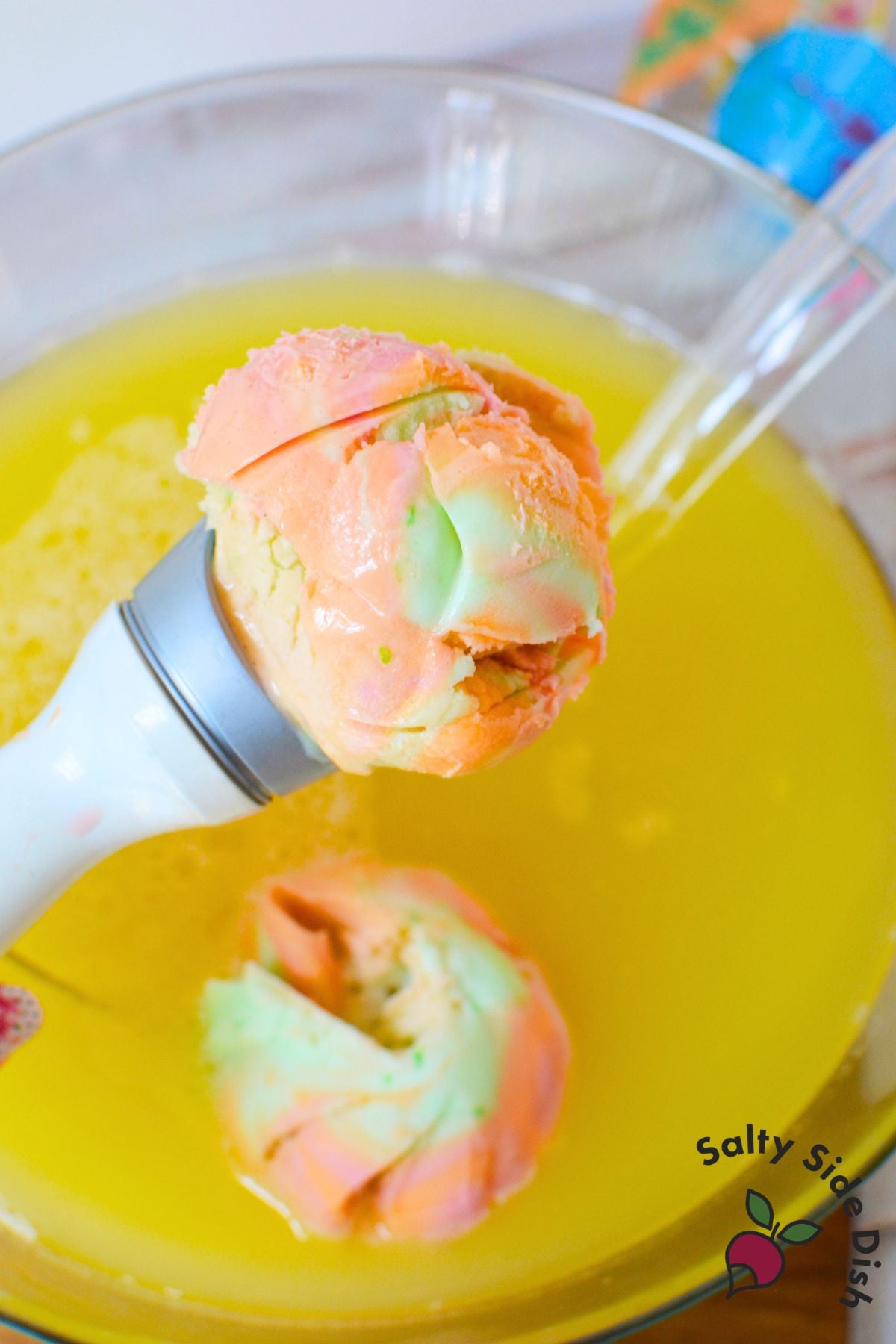 Scoop of rainbow sherbet added to pineapple juice and lemon-lime soda in a punch bowl
