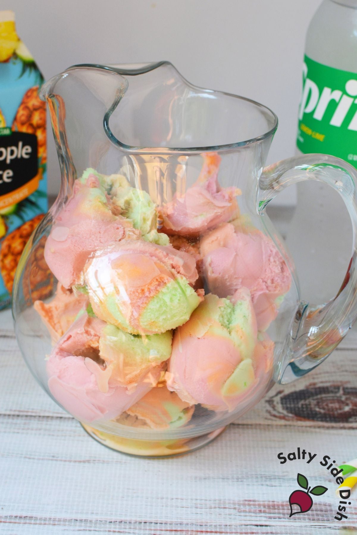 Rainbow sherbet scoops packed into a glass pitcher for sherbet party punch