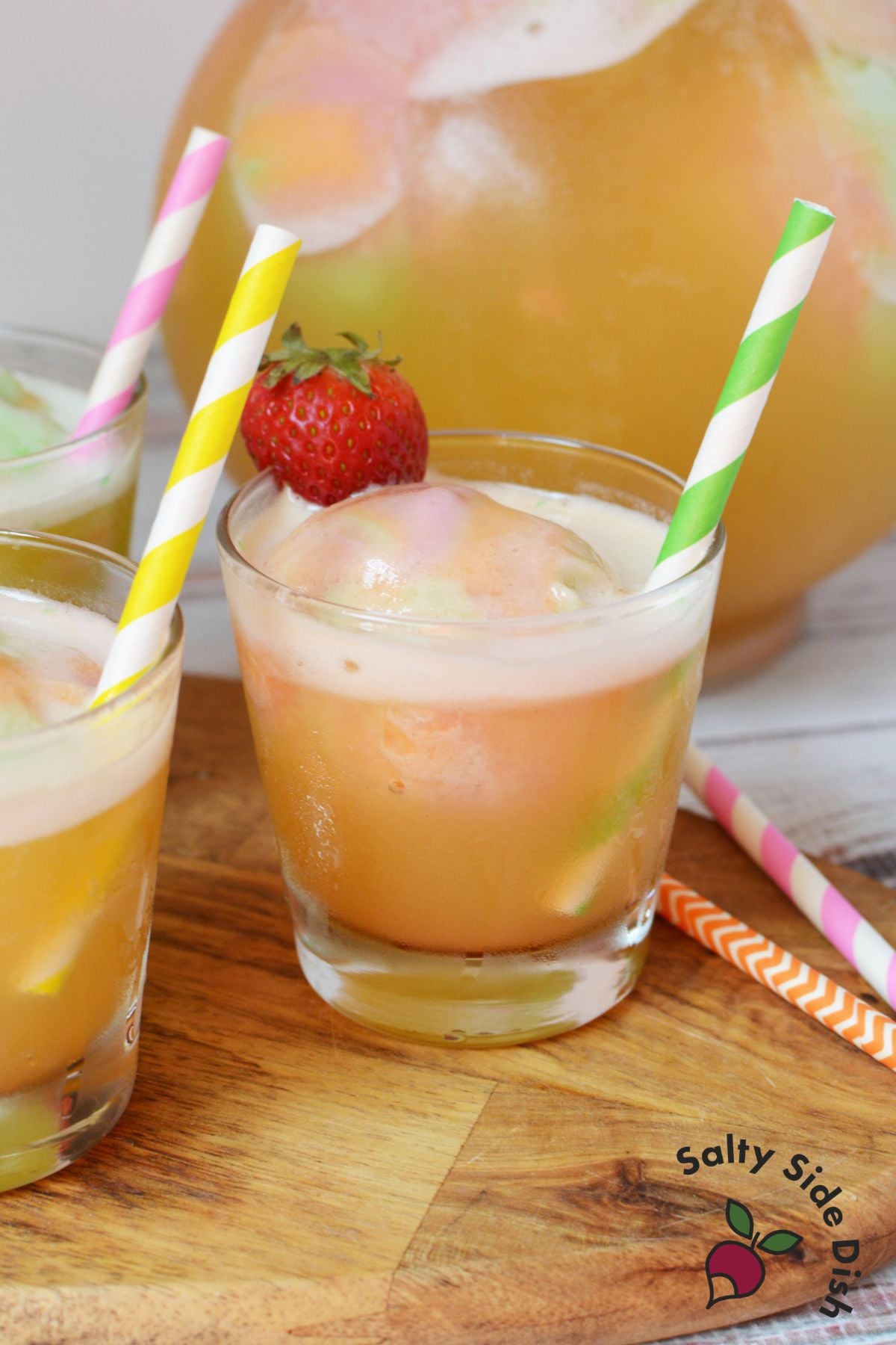 Easy rainbow sherbet punch served in glasses with strawberries and colorful paper straws
