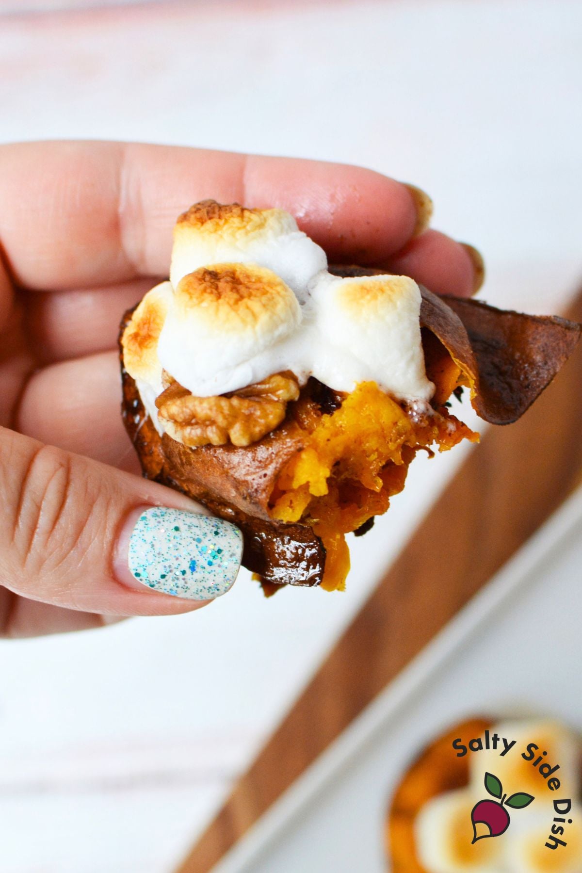 Close-up of handheld smashed sweet potato with crispy skin, pecans, and toasted marshmallows