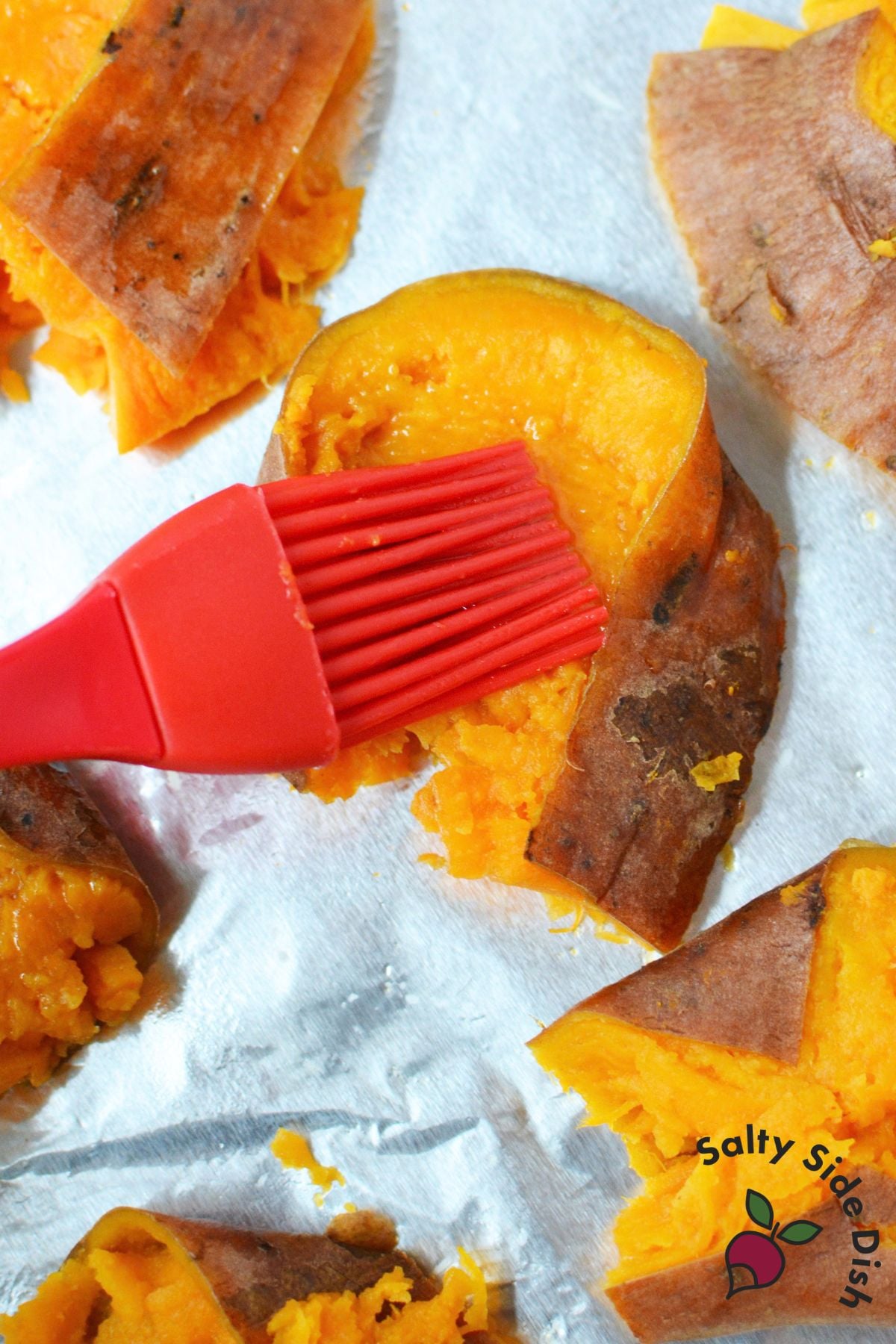 Olive oil being brushed over smashed sweet potatoes before roasting