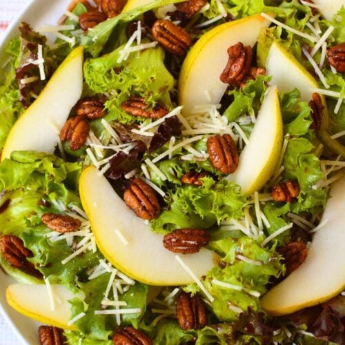 Fall pear salad topped with thinly sliced pears, toasted pecans, Parmesan cheese, and balsamic dressing