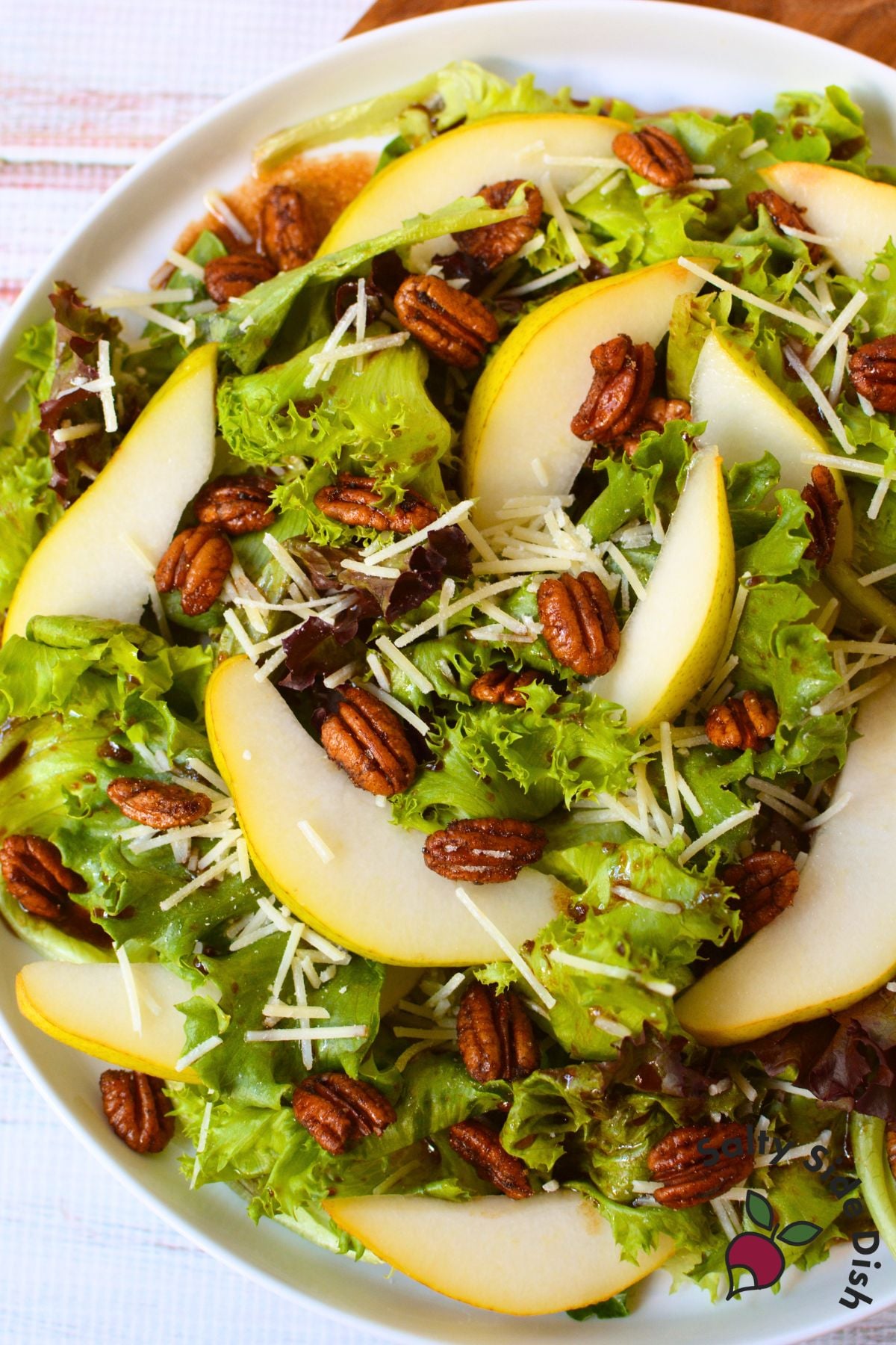 Fall pear salad topped with thinly sliced pears, toasted pecans, Parmesan cheese, and balsamic dressing