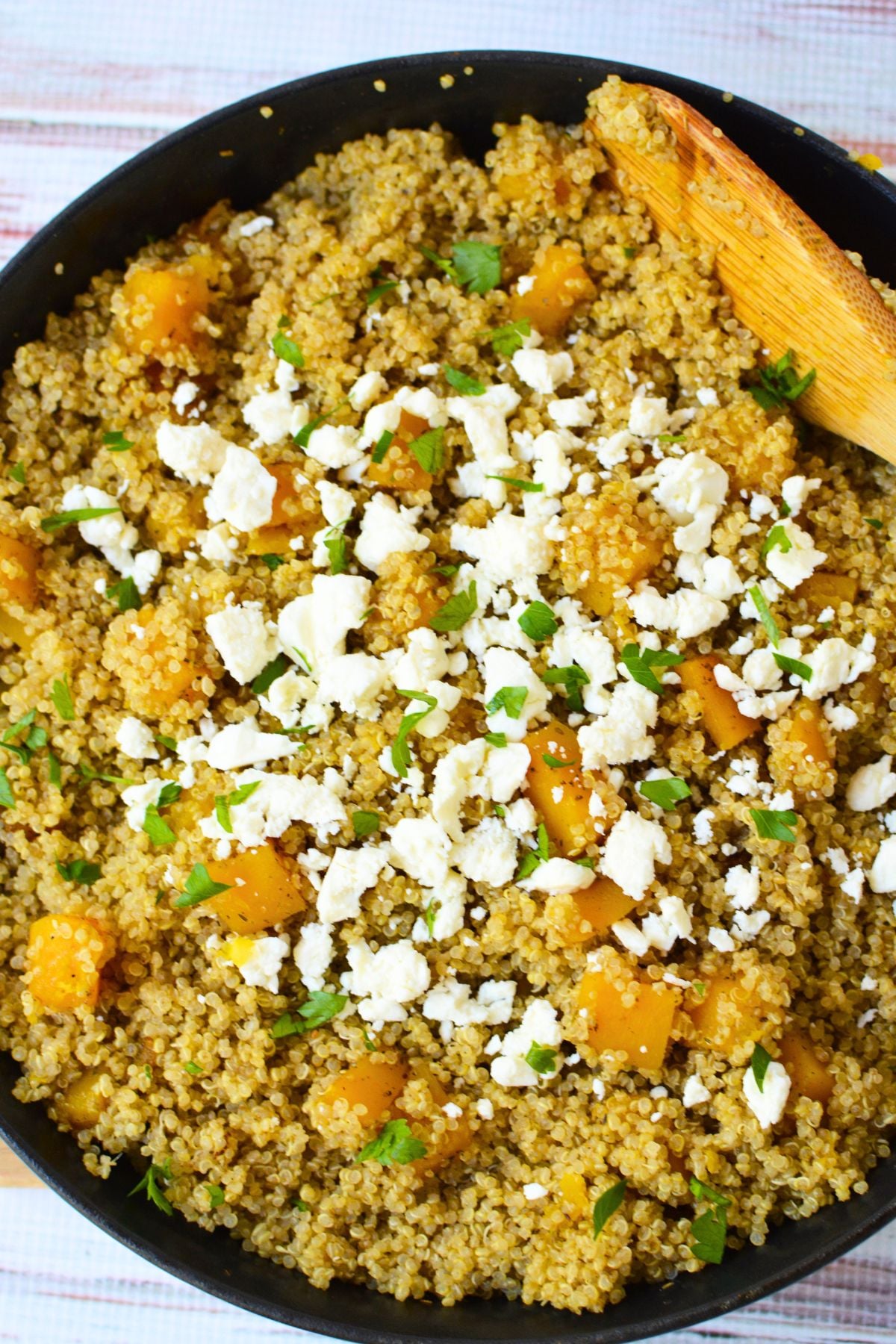Warm butternut squash quinoa salad with cumin-seasoned quinoa, tender squash cubes, crumbled feta cheese, and fresh parsley in a skillet.
