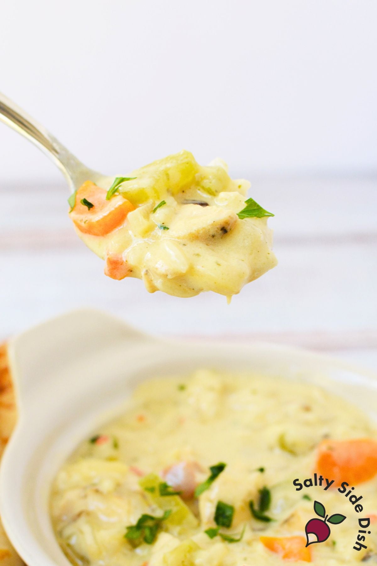 Close-up of a spoonful of chicken wild rice soup with chicken, carrots, celery, and creamy broth