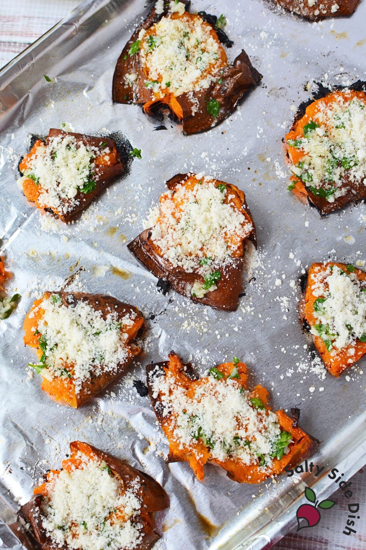 Garlic Parmesan smashed sweet potatoes on a foil-lined baking sheet topped with parsley and grated Parmesan.