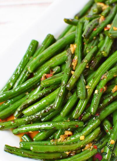 Honey garlic green beans served on a white platter with visible garlic and red pepper flakes.