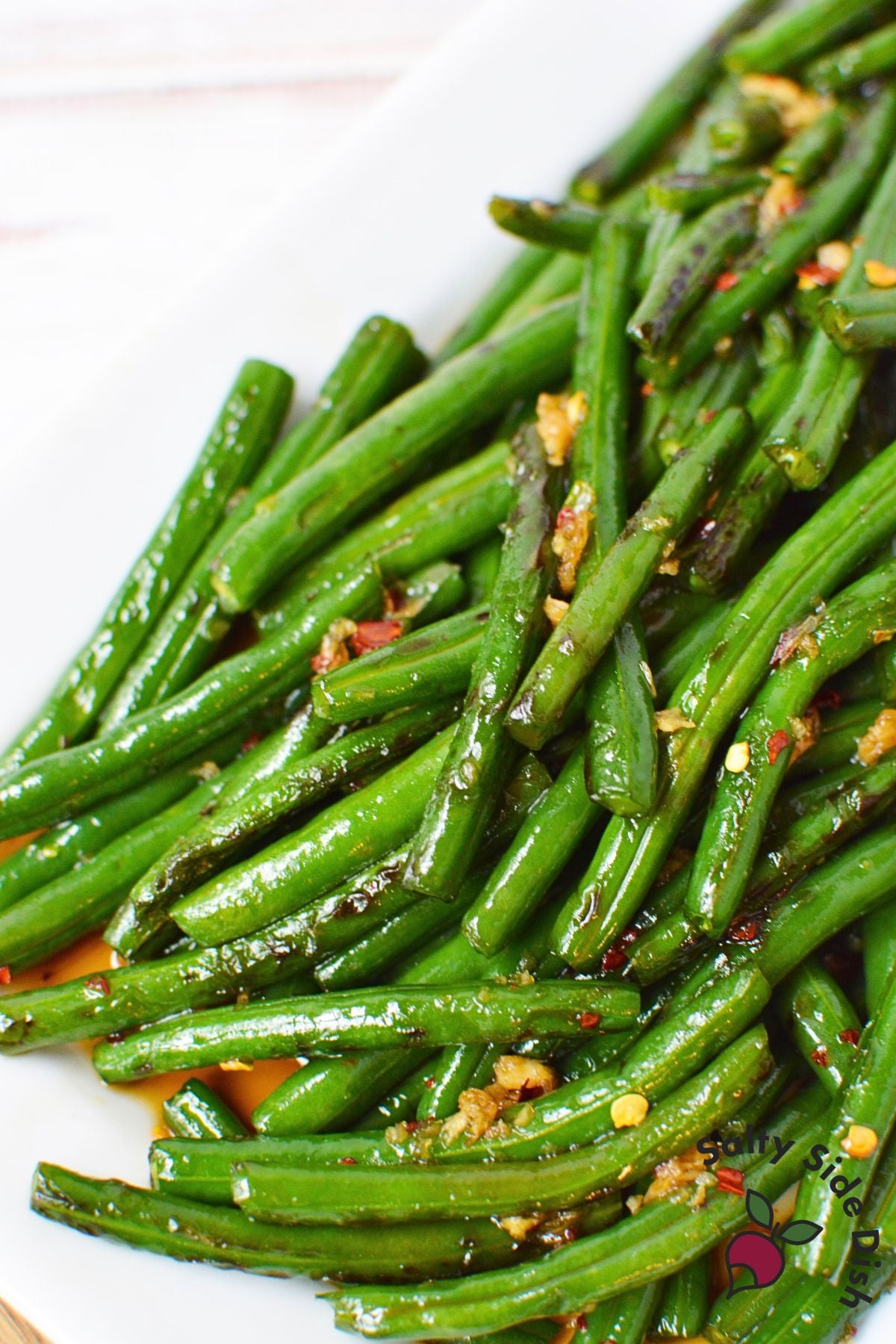 Honey garlic green beans served on a white platter with visible garlic and red pepper flakes.